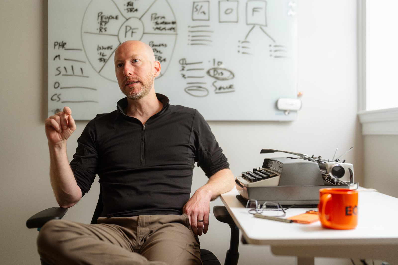 Dennis at a whiteboard mapping EOS components, a typewriter and orange EOS mug on the desk